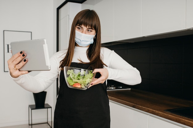 Blogger femenina grabando a sí misma con tableta mientras prepara ensalada