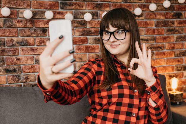 Blogger femenina que fluye en línea con el teléfono inteligente y da la señal de bien