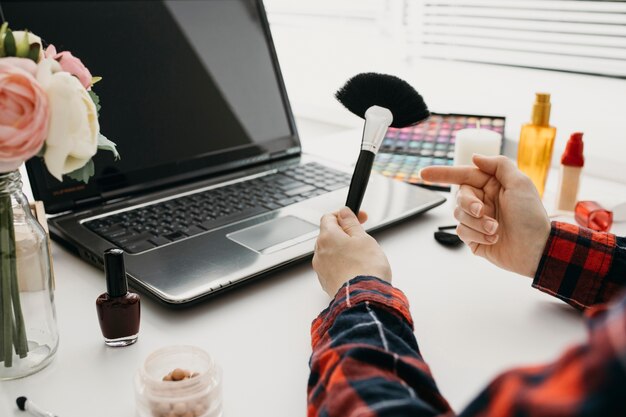 Blogger femenina que transmite pinceles de maquillaje en línea con un portátil