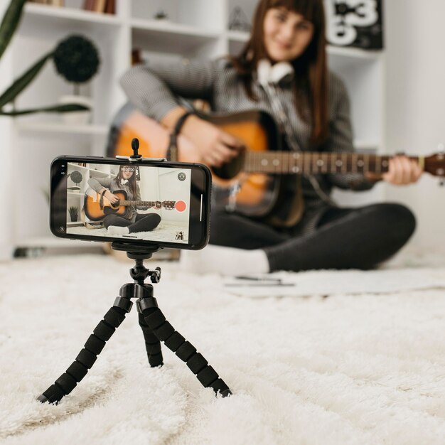 Blogger femenino streaming lecciones de guitarra con cámara smartphone en casa