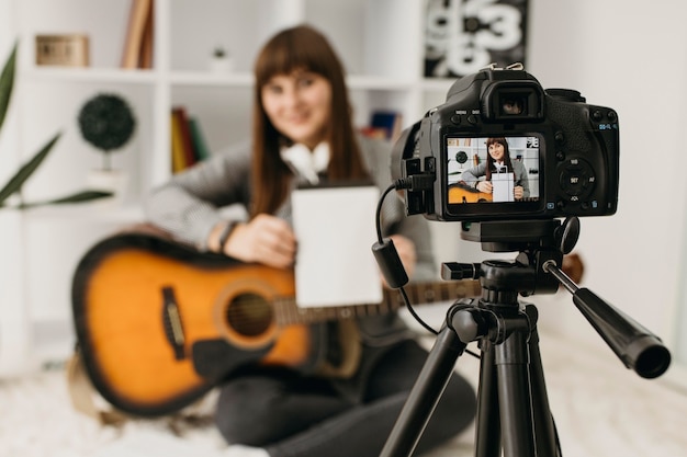 Blogger femenino streaming lecciones de guitarra en casa con cámara