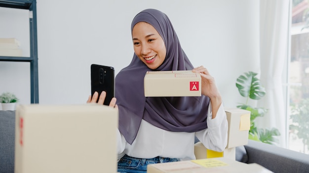 Blogger joven empresaria musulmana que usa la cámara del teléfono móvil para grabar el producto de revisión de transmisión en vivo de video vlog en la oficina en casa.
