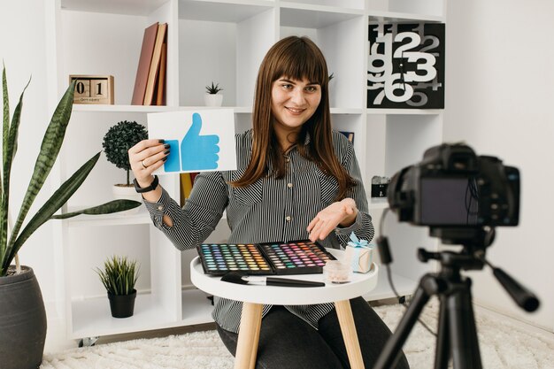 Blogger de maquillaje femenino sonriente con streaming en casa con cámara