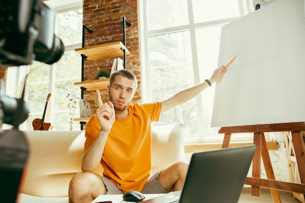 Blogger masculino caucásico joven con revisión de video de grabación de cámara profesional de gadgets en casa