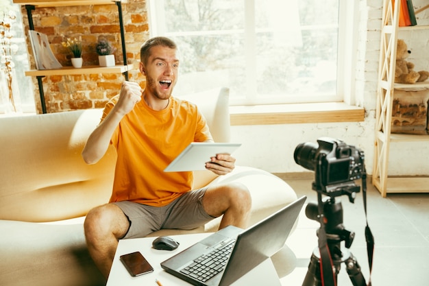 Blogger masculino caucásico joven con revisión de video de grabación de cámara profesional de tableta en casa