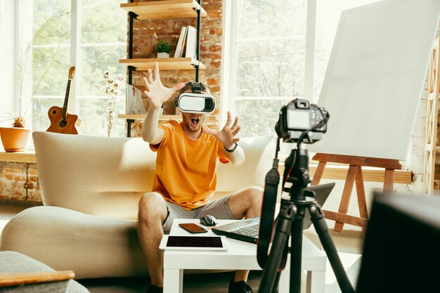 Blogger masculino caucásico joven con revisión de video de grabación de equipo profesional de gafas VR en casa. Blogs, videoblogs, vlogs. Hombre usando casco de realidad virtual mientras transmite en vivo.