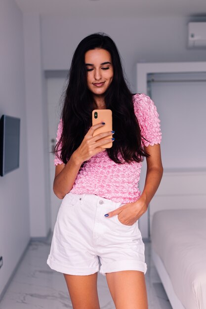 Blogger de moda joven bastante caucásica vistiendo ropa elegante, tomando foto selfie