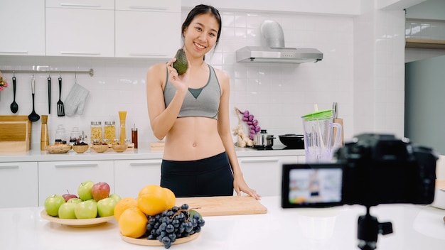 Blogger mujer asiática deportiva con cámara grabando cómo hacer un video de jugo de aguacate para su suscriptor