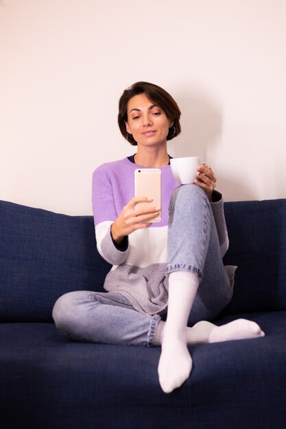 Blogger de mujer linda caucásica en casa en suéter de suéter púrpura cálido tomar selfie en espejo en el teléfono móvil