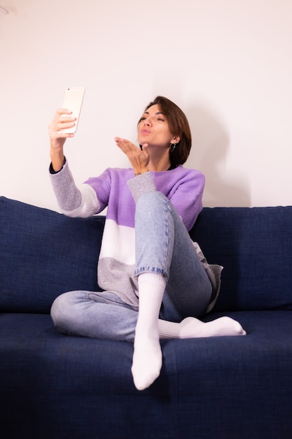 Blogger de mujer linda caucásica en casa en suéter de suéter púrpura cálido tomar selfie en espejo en el teléfono móvil
