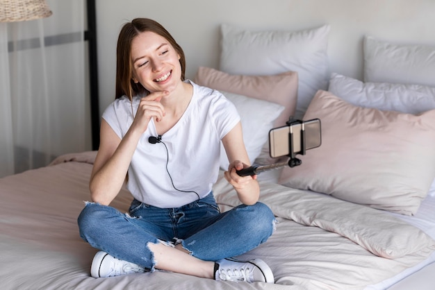 Foto gratuita blogger sentada en la cama y grabándose a sí misma