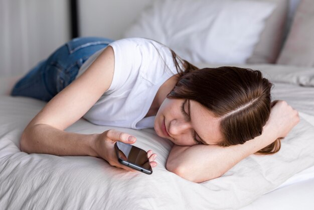 Blogger soñolienta en la cama usando su teléfono inteligente
