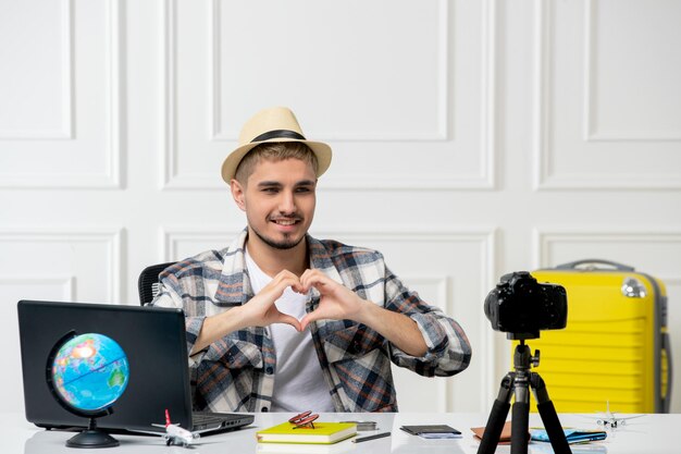 Blogger de viajes grabando vlog de viaje en cámara joven guapo con sombrero de paja enviando amor