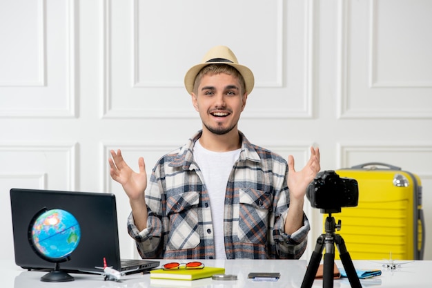 Blogger de viajes guapo joven grabando vlog de viaje en cámara con equipaje amarillo agitando las manos