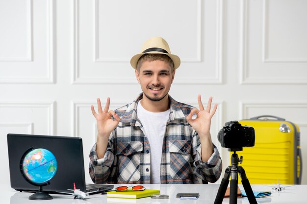 Blogger de viajes guapo joven grabando vlog de viaje en cámara con equipaje amarillo en paja