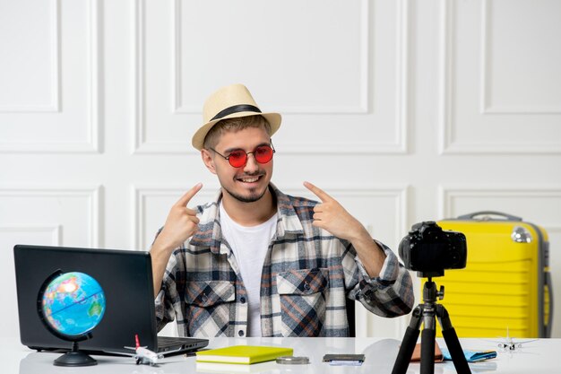 Blogger de viajes con sombrero de paja joven guapo grabando vlog de viaje en cámara con gafas rojas