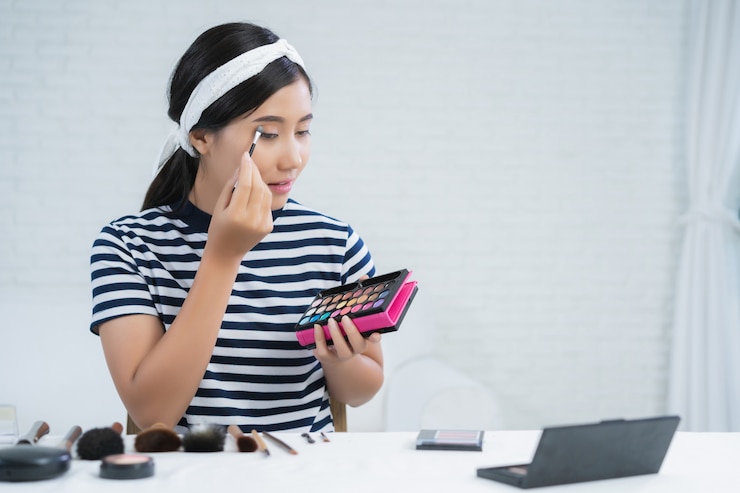 Foto gratuito la bloguera de belleza presenta cosméticos de belleza mientras se sienta frente a la cámara para grabar video