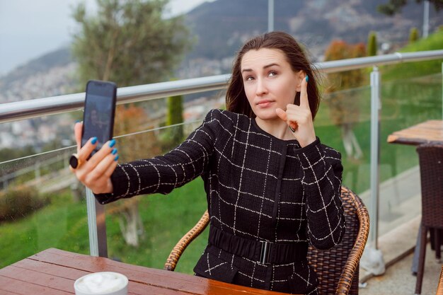 La bloguera pensante se está tomando una selfie con la cámara trasera del teléfono inteligente señalando el fondo de la vista de la naturaleza