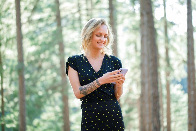 La bloguera sonriente está chateando en el móvil sobre el fondo de la naturaleza