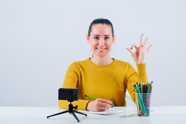 Una bloguera sonriente está mostrando un gesto correcto al sentarse en un fondo blanco