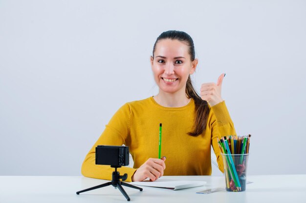 Una bloguera sonriente sostiene un lápiz y muestra un gesto perfecto con la otra mano en el fondo blanco