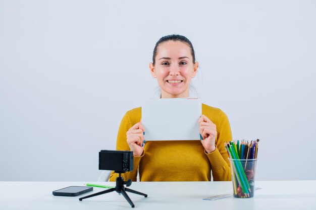 Una bloguera sonriente sostiene un libro blanco mirando a la cámara con fondo blanco