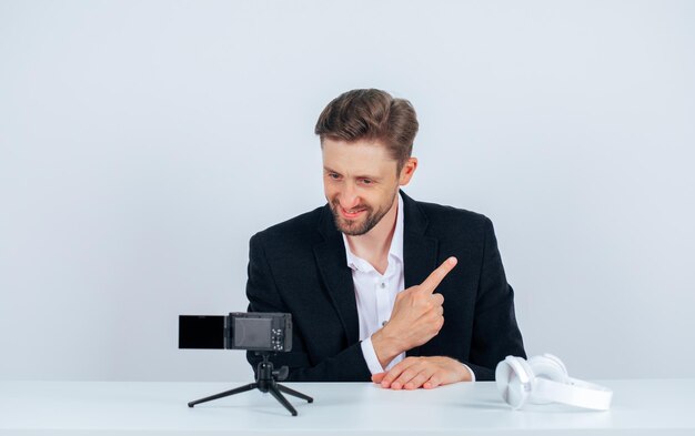 Un bloguero sonriente posa para su mini cámara apuntando hacia la derecha con el dedo índice sobre fondo blanco