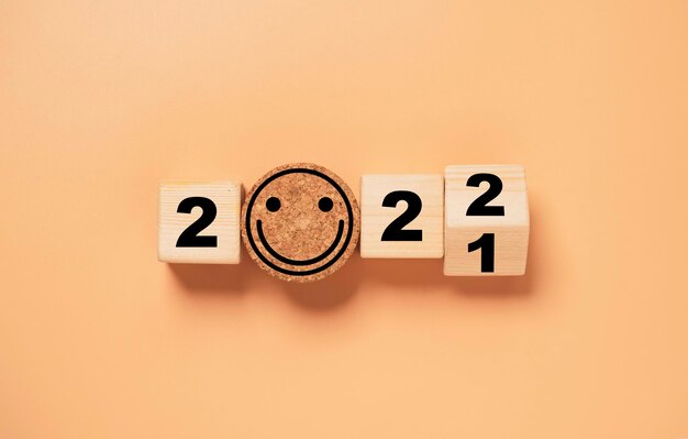 Bloque de cubo de madera volteando de 2021 a 2022 con cara de sonrisa sobre fondo naranja, preparación para feliz navidad y próspero año nuevo y concepto de representación 3d. Foto Premium 