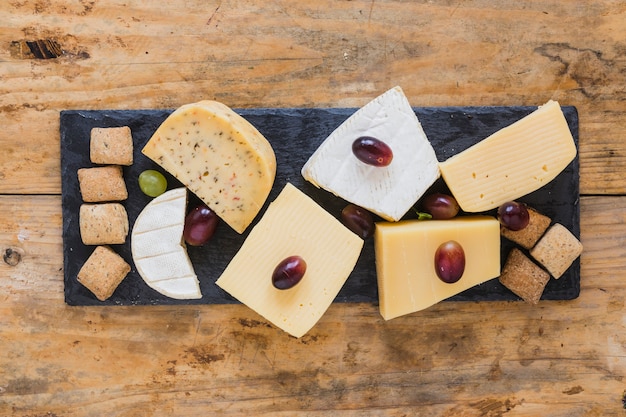 Foto gratuita bloque de queso con uvas y pastelería en un plato de pizarra sobre el escritorio de madera