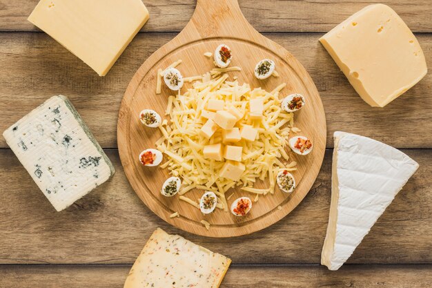 Bloques de queso rodeados cerca de la tabla de cortar de madera en el escritorio de madera