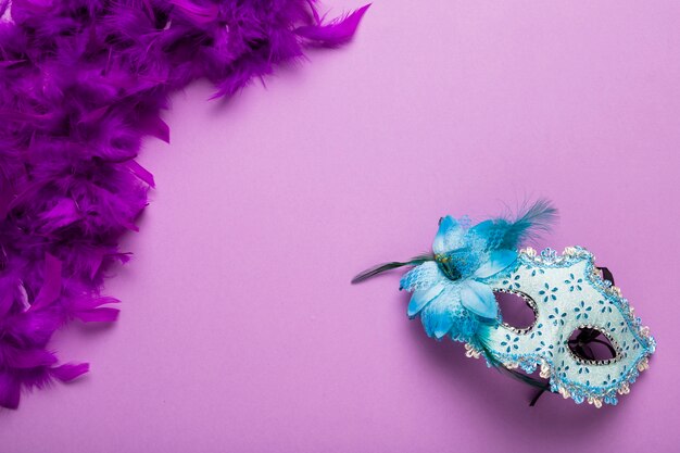 Boa de plumas morada con máscara de carnaval azul y espacio de copia