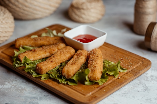 Bocaditos crujientes de pollo, palitos con ketcup sobre una tabla de madera con cestas rústicas alrededor