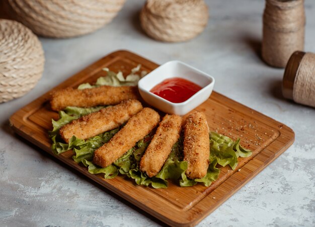 Bocaditos crujientes de pollo, palitos con ketcup sobre una tabla de madera