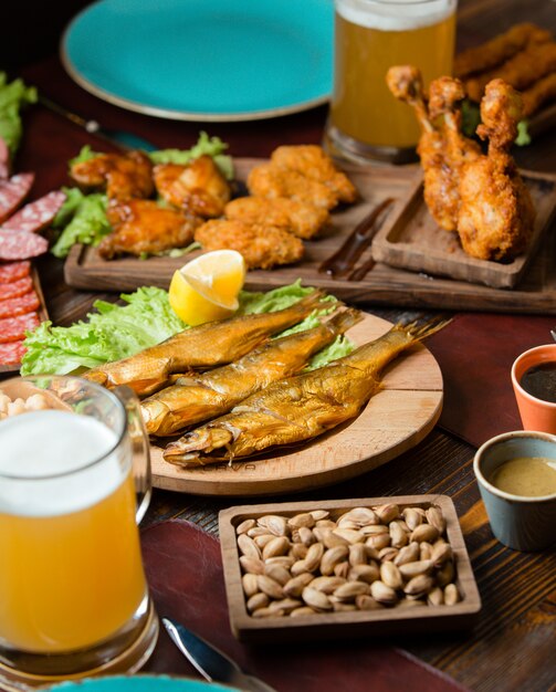 Bocaditos de pescado seco, nuggets de pollo y pistachos con un vaso de cerveza.