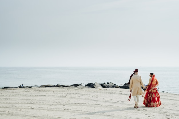 Boda hindú pareja camina a lo largo de la costa del océano