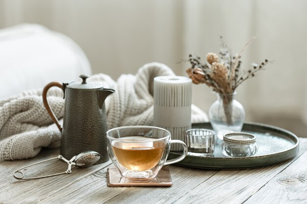 Bodegón acogedor con una taza de té, una tetera y velas sobre un fondo borroso.