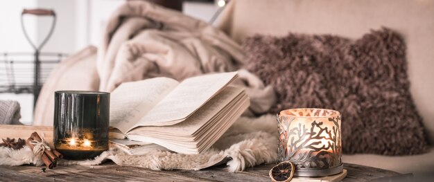 Bodegón ambiente hogareño en el interior con un libro y velas, sobre la mesa de colchas acogedoras