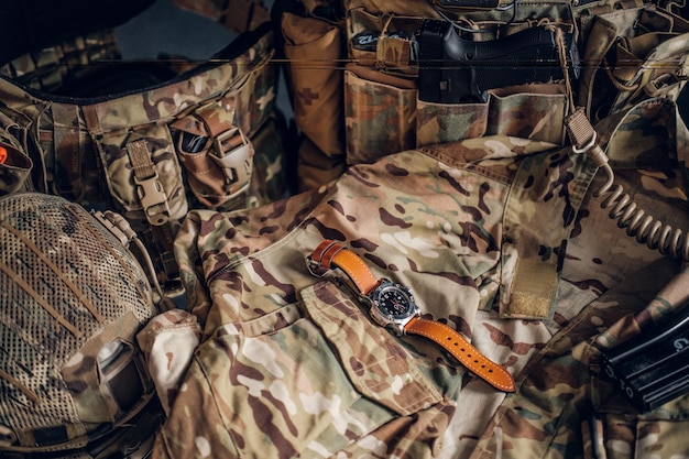 Bodegón con bonito reloj y uniforme militar con patrón de camuflaje típico.