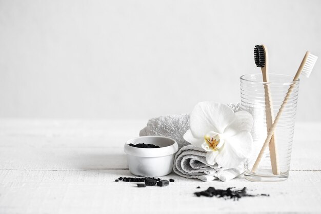 Bodegón con cepillos de bambú orgánico y polvo de carbón activado y una flor de orquídea como elemento decorativo. Higiene bucal y cuidado dental.