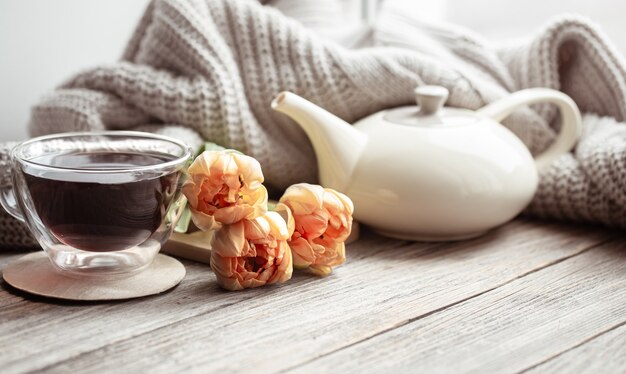 Bodegón festivo con flores, una taza de té y una tetera sobre una superficie de madera de cerca.