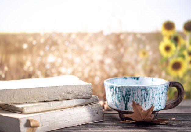 Bodegón otoñal con libros y una hermosa taza en el fondo borroso de un campo y girasoles.