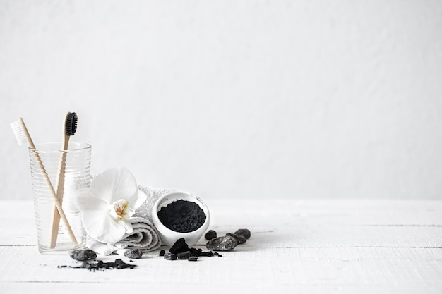 Bodegón con pinceles de bambú orgánico y polvo de carbón activado y una flor de orquídea como elemento decorativo. Antecedentes de higiene bucal y cuidado dental.