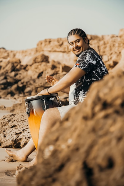 Boho musuciano en una playa abandonada con su tambor