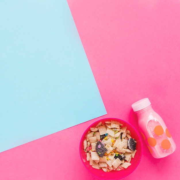 Bol con cereales y botella de leche rosa.