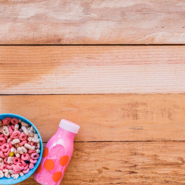 Bol con cereales y botella de leche rosa.