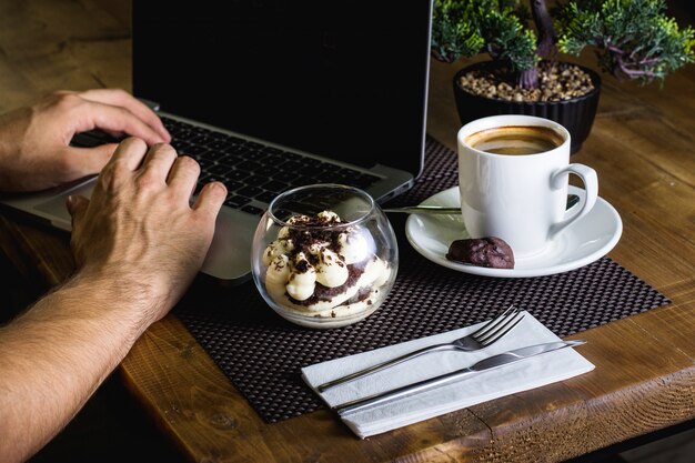 Un bol de cristal de tiramisú y una taza de café expreso servido para el hombre que trabaja en su cuaderno