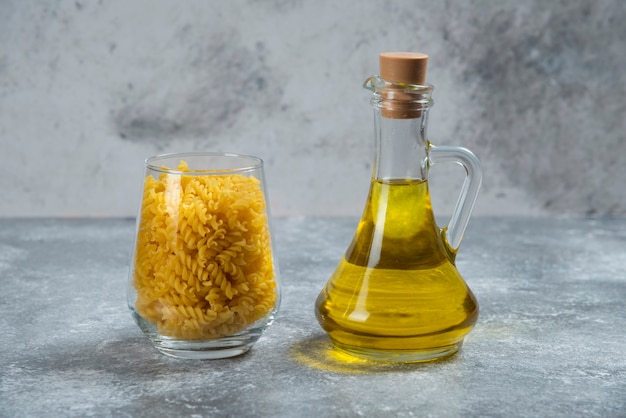 Un bol de vidrio con macarrones crudos en espiral con una botella de aceite.