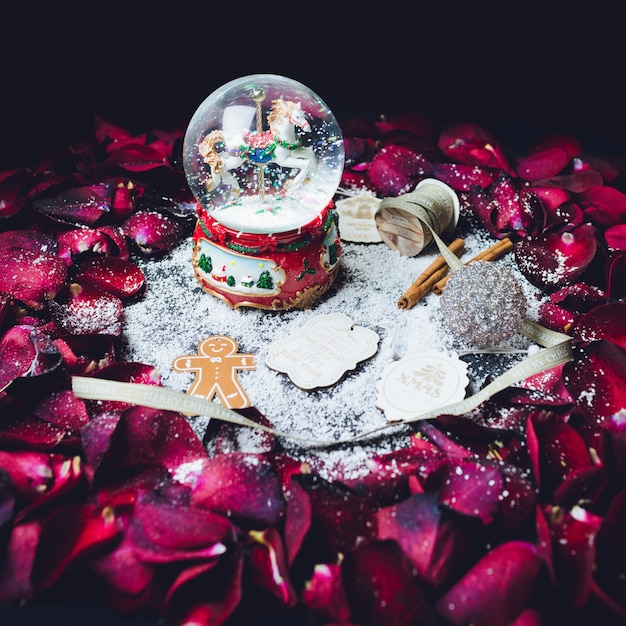 Bola de cristal con nieve y otros elementos de decoración de Navidad en el círculo de pétalos de rosas rojas