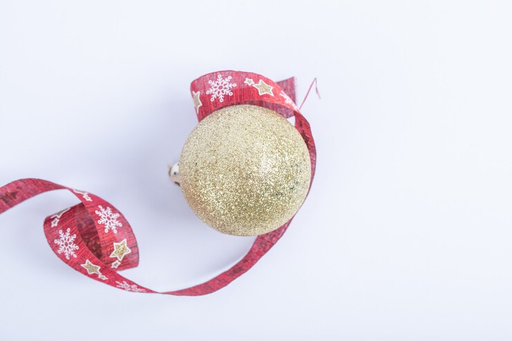 Foto gratuito una bola dorada brillante con cinta roja de navidad sobre el blanco.