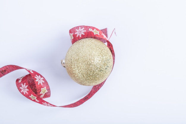 Una bola dorada brillante con cinta roja de Navidad sobre el blanco.